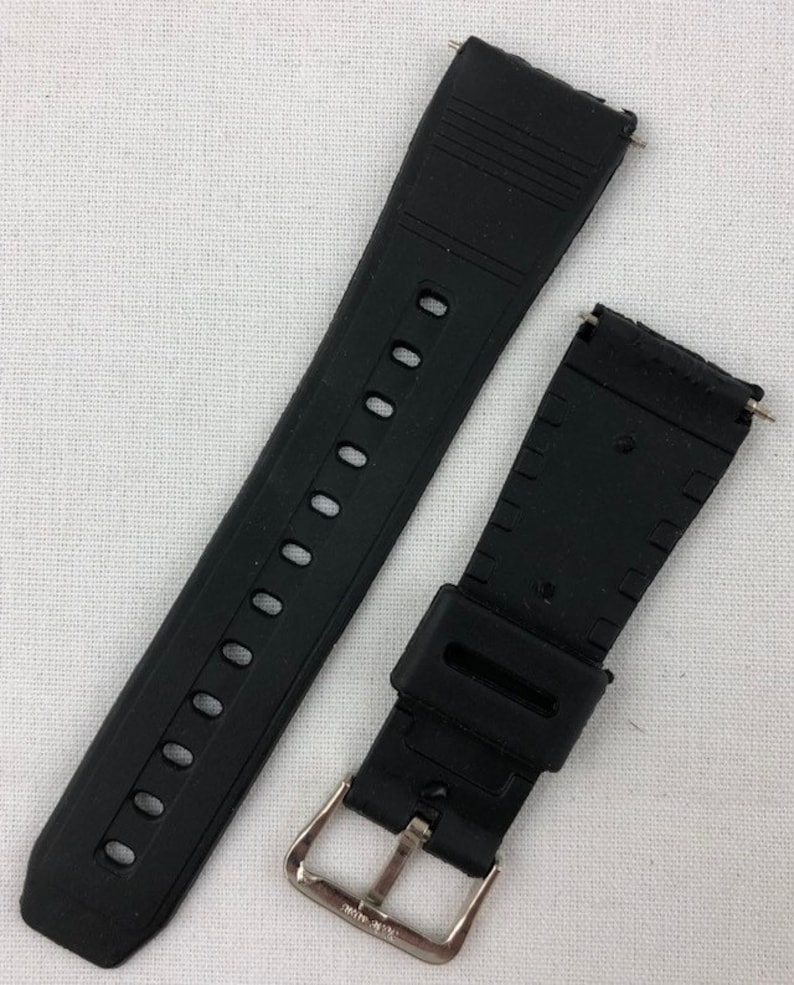 Puede incluir: Correa de reloj de goma negra con hebilla plateada. La correa tiene una superficie texturizada y est&aacute; dise&ntilde;ada para un reloj de pulsera.