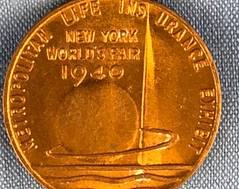 Könnte beinhalten: Eine bronzefarbene Münze mit der Aufschrift "LIFE INSURANCE NEW YORK WORLD'S FAIR 1940", die ein Segelboot-Design umgibt. Die Münze enthält auch die Worte "METROPOLITAN EXHIBIT".