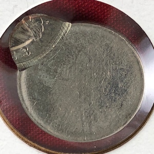 May include: A silver US quarter coin with a red border, the coin is damaged and missing a portion of the edge.