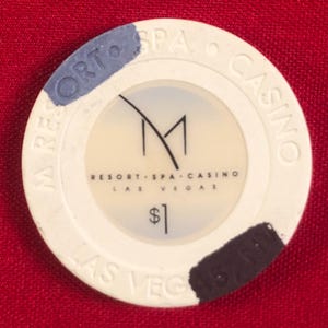 May include: A white casino chip with a black and gray design. The chip has the text "M Resort Spa Casino Las Vegas" and "$1" printed on it.