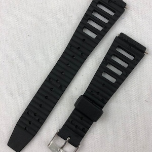 May include: Black rubber watch band with a silver buckle. The band has a textured surface and a series of holes for ventilation.