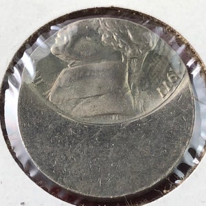 May include: Close-up of a silver coin with a profile of a person on the front and the year 1965 on the back.