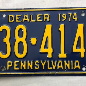 May include: A blue and yellow Pennsylvania dealer license plate from 1974 with the number B38-414B.
