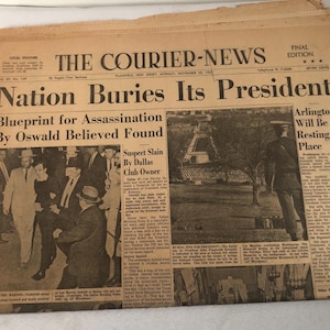 May include: A black and white newspaper headline reads "Nation Buries Its President". The headline is accompanied by a photo of a group of people in suits and a photo of a grassy area. The newspaper is dated November 23, 1963.