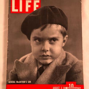 May include: A vintage LIFE magazine cover featuring a black and white portrait of a young boy wearing a dark beret and coat. The cover text reads "LIFE" in white letters on a red background, with "GENERAL MACARTHUR'S SON" below.