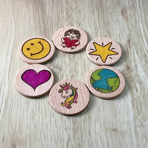 K&ouml;nnte beinhalten: Sechs Holz-Kreise mit verschiedenen Designs, darunter ein Smiley, ein Herz, ein Igel, der ein Herz h&auml;lt, ein Stern, ein Globus und ein Einhorn. Die Kreise sind in einem Kreis auf einer Holzoberfl&auml;che angeordnet.