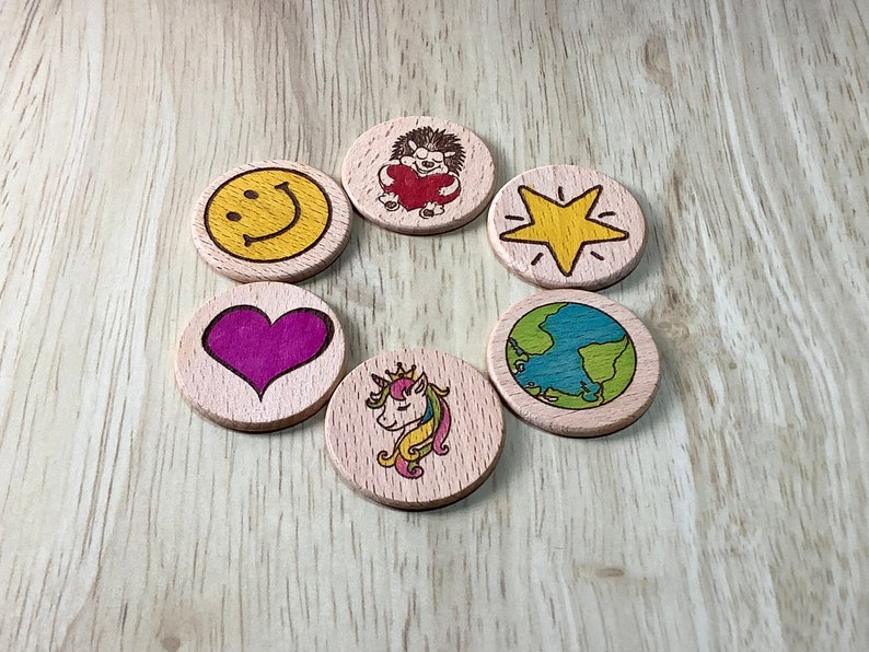 K&ouml;nnte beinhalten: Sechs Holz-Kreise mit verschiedenen Designs, darunter ein Smiley, ein Herz, ein Igel, der ein Herz h&auml;lt, ein Stern, ein Globus und ein Einhorn. Die Kreise sind in einem Kreis auf einer Holzoberfl&auml;che angeordnet.