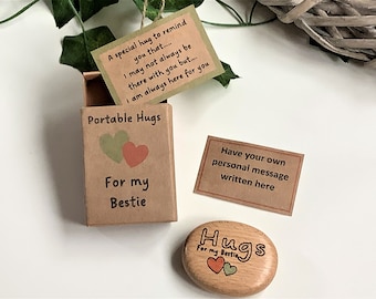 May include: A small wooden box with a message inside that reads "A special hug to remind you that... I may not always be there with you but... I am always here for you." The box is labeled "Portable Hugs" and "For my Bestie". A small wooden heart-shaped hug stone is also shown with the text "Hugs" and "For my Bestie".