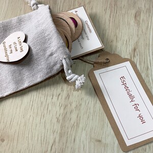 K&ouml;nnte beinhalten: Ein kleiner Jutesack gef&uuml;llt mit Holztoken und einem herzf&ouml;rmigen Holzschild mit der Aufschrift "Ein kleiner Beutel voller Liebe f&uuml;r meine Enkelin". Ein braunes Schild mit dem Text "Speziell f&uuml;r dich" ist am Sack befestigt.