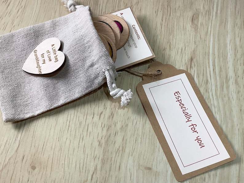 K&ouml;nnte beinhalten: Ein kleiner Jutesack gef&uuml;llt mit Holztoken und einem herzf&ouml;rmigen Holzschild mit der Aufschrift "Ein kleiner Beutel voller Liebe f&uuml;r meine Enkelin". Ein braunes Schild mit dem Text "Speziell f&uuml;r dich" ist am Sack befestigt.