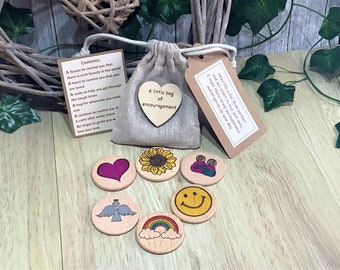 May include: A small burlap bag with a heart-shaped tag that reads "A little bag of encouragement". The bag contains wooden tokens with various images, including a heart, sunflower, angel, rainbow, and smiley face. The tokens are meant to be uplifting and encouraging.