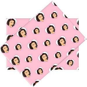 Puede incluir: Papel de regalo rosa con un patrón repetido de un rostro dentro de un corazón blanco. La persona tiene cabello largo y castaño y sostiene un micrófono. Un lazo rosa está en la cabeza de la persona.