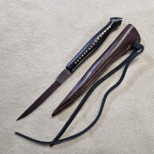 May include: A small black handled knife with a brown leather sheath and a black leather strap. The handle is decorated with gold dots.