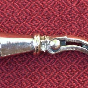 May include: A silver-coloured metal bottle stopper with a unique design. The stopper has a cylindrical base and a curved, beak-like spout.