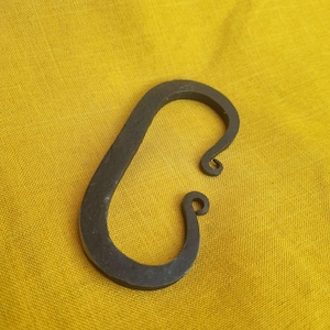 May include: A black metal fire starter with a curved shape and two loops at the top. The fire starter is on a yellow fabric background.