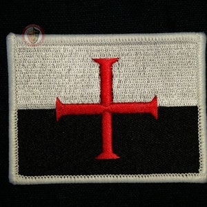 May include: A white and black embroidered patch with a red cross. The patch is surrounded by a white border.
