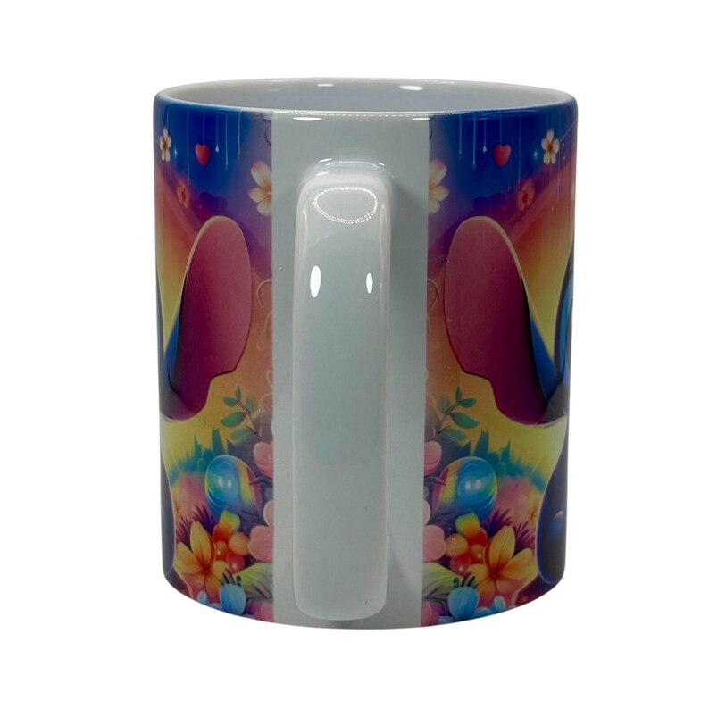 May include: White ceramic mug featuring a colorful cartoon character design. The mug has a white handle and a vibrant wrap-around design with flowers, hearts, and a character's face. The background transitions from blue to yellow.