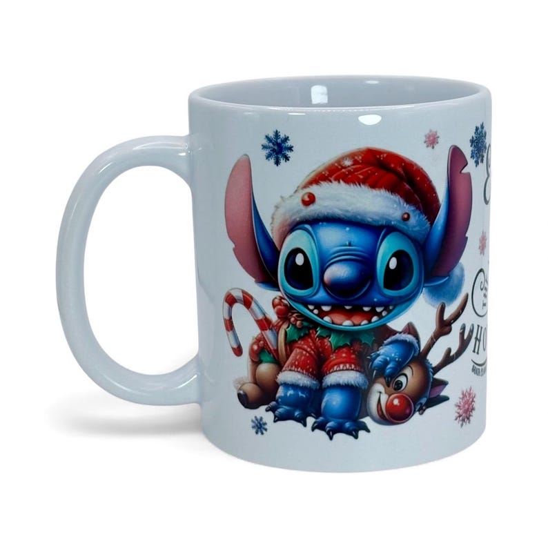 May include: White ceramic mug featuring a blue cartoon character wearing a Santa hat and Christmas sweater. The mug has a candy cane and reindeer design, with snowflakes and the text "Merry Christmas".