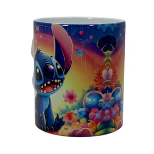 May include: A ceramic mug featuring a colorful illustration of a blue cartoon character with large ears and a wide grin. The mug is decorated with flowers, butterflies, and a rainbow-colored background. The mug is white on the inside.