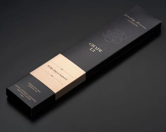 Può includere: Scatola rettangolare nera di incenso con testo dorato "GRADE 1.3" e "PURE PALO SANTO". La scatola presenta una fascia beige al centro e le parole "LONDON" e "CREATED WITH PURE ESSENTIAL OILS".