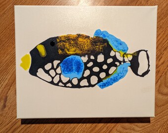 May include: A black, white, yellow, and blue abstract painting of a fish on a white canvas.