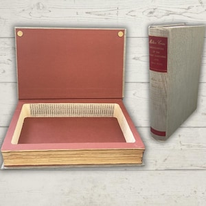 May include: A vintage book transformed into a hidden storage box. The open box reveals a hollowed-out interior with a red-brown interior and a light-colored exterior. A second book with a red spine is next to the box.