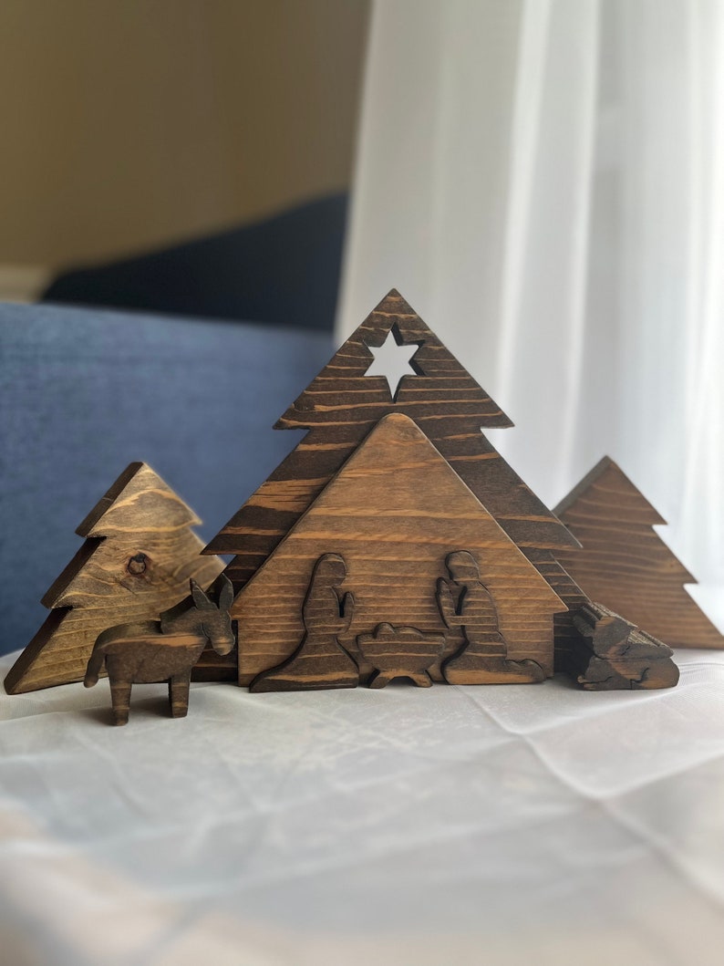 May include: Wooden Christmas nativity scene with a brown wooden stable, two trees, a donkey, and figures of Mary, Joseph, and baby Jesus.