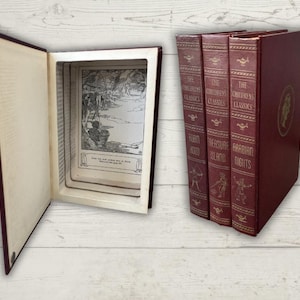 Puede incluir: Un libro hueco de color burdeos con un compartimento abierto que revela una ilustración en blanco y negro. Junto a él, tres libros burdeos a juego con letras e ilustraciones doradas, titulados "The Children's Classics: Robin Hood, Treasure Island, Arabian Nights."