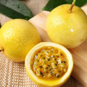 May include: Three yellow passion fruits, one cut open to reveal the pulp with black seeds. The fruit is on a wooden cutting board and a textured surface. The passion fruit has a smooth, shiny skin.