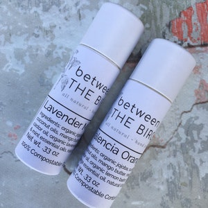 May include: Two white tubes of natural body balm with labels that read "between the birds" and the names of the scents, "Lavender" and "Valencia Orange". The tubes are 0.33 oz and 100% compostable.