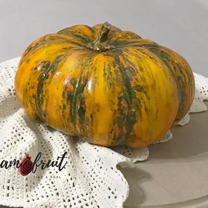Könnte beinhalten: Ein Keramik-Kürbis mit glänzender Oberfläche in leuchtendem Gelb und Orange, akzentuiert durch dunkelgrüne vertikale Streifen und einen strukturierten Stiel. Der Text Ceramfruit LIKE A REAL ist in Schwarz und Rot auf dem Spitzenstoff gedruckt.