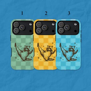 May include: Three phone cases with a raccoon design. Each case has a different background colour: green, yellow, and blue. The raccoon illustration is in a vintage style, with its arms raised. The cases are designed for a smartphone.