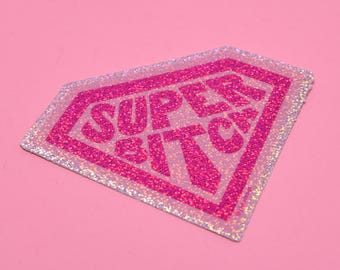 May include: Pink glitter iron-on patch with the text "SUPER BITCH" in a diamond shape.