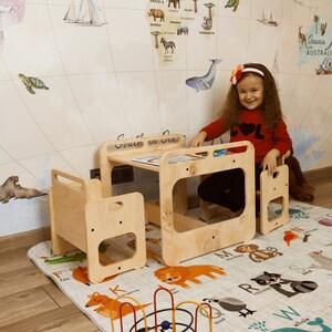 Puede incluir: Una ni&ntilde;a peque&ntilde;a se sienta en un conjunto de mesa y silla de madera para ni&ntilde;os. La mesa tiene un peque&ntilde;o estante debajo y la silla tiene un dise&ntilde;o recortado. El conjunto est&aacute; en una habitaci&oacute;n con un papel tapiz de mapa del mundo y una alfombra de alfabeto colorida.