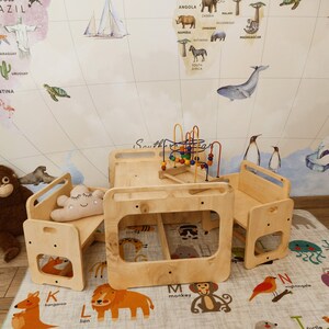 Puede incluir: Una mesa de juego de madera con dos bancos unidos y un laberinto de cuentas de colores en el centro. La mesa y los bancos son de color madera natural. La mesa est&aacute; sobre una alfombra con ilustraciones de animales y letras.