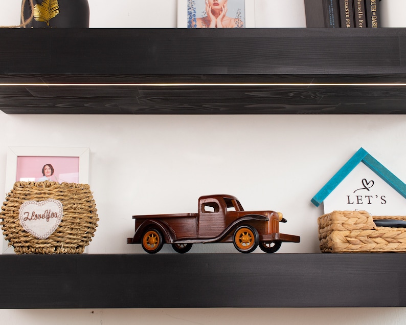 K&ouml;nnte beinhalten: Ein Holzmodell eines Oldtimer-Pickups mit orangefarbenen R&auml;dern und brauner Karosserie steht auf einem schwarzen Regal. Das Regal enth&auml;lt auch einen geflochtenen Korb mit einem herzf&ouml;rmigen Aufn&auml;her mit der Aufschrift "I Love You".