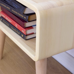 May include: A light wood end table with rounded edges and four legs. The table has a shelf that is holding a stack of five books.