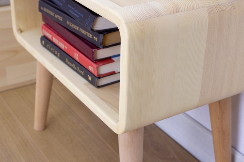 May include: A light wood end table with rounded edges and four legs. The table has a shelf that is holding a stack of five books.