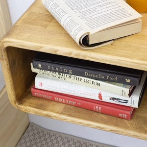 K&ouml;nnte beinhalten: Ein Wandregal aus Holz mit einer abgerundeten Vorderkante. Das Regal enth&auml;lt einen Stapel B&uuml;cher, darunter "The Sword of the Lictor" von Gene Wolfe und "Rising" von Darnella Ford. Au&szlig;erdem befindet sich eine kleine Topfpflanze auf dem Regal.