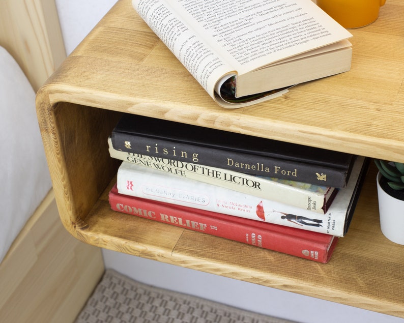 K&ouml;nnte beinhalten: Ein Wandregal aus Holz mit einer abgerundeten Vorderkante. Das Regal enth&auml;lt einen Stapel B&uuml;cher, darunter "The Sword of the Lictor" von Gene Wolfe und "Rising" von Darnella Ford. Au&szlig;erdem befindet sich eine kleine Topfpflanze auf dem Regal.