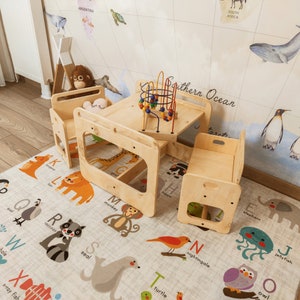 Puede incluir: Un conjunto de juegos de madera con dos sillas y una mesa. La mesa tiene un juguete colorido en la parte superior. El conjunto de juegos est&aacute; en una alfombra de juegos con un alfabeto e ilustraciones de animales.