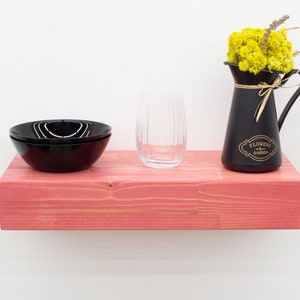 May include: A pink wooden shelf with a black glass bowl, a clear glass, and a black pitcher with yellow flowers and the text "Flowers & Garden".