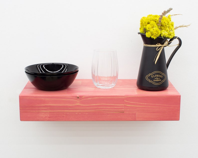 May include: A pink wooden shelf with a black glass bowl, a clear glass, and a black pitcher with yellow flowers and the text "Flowers & Garden".