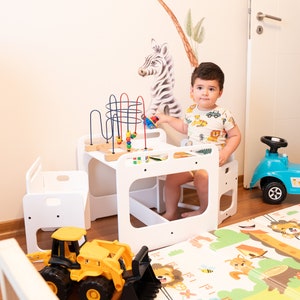 May include: A white wooden table and chair set for children, with a colorful bead maze and a toy tractor on the floor. The set is designed for toddlers and preschoolers.