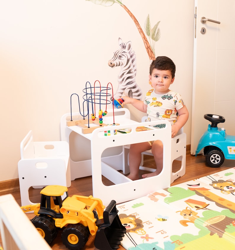 May include: A white wooden table and chair set for children, with a colorful bead maze and a toy tractor on the floor. The set is designed for toddlers and preschoolers.