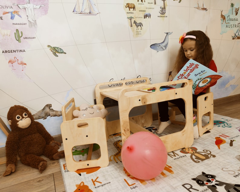 Puede incluir: Un juego de mesa y sillas de madera clara para ni&ntilde;os con un globo rosa en el suelo. La mesa tiene un peque&ntilde;o estante debajo y las sillas tienen un respaldo peque&ntilde;o y un recorte para los pies de un ni&ntilde;o. Un ni&ntilde;o est&aacute; sentado en la mesa leyendo un libro titulado "&Ccedil;ikolatalı Kurabiye".