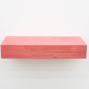 May include: A solid wood shelf painted a bright pink color. The shelf is made of natural wood with visible grain.