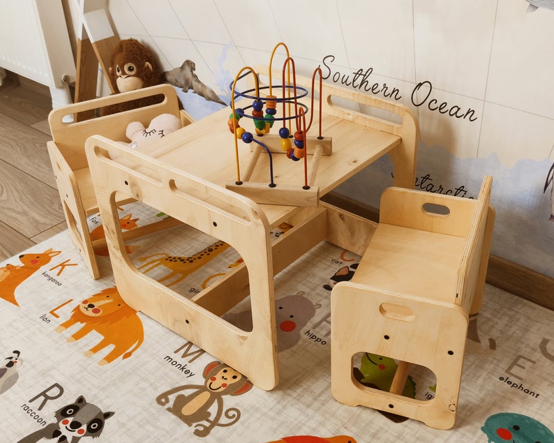 Puede incluir: Un juego de mesa y sillas de madera para ni&ntilde;os. La mesa tiene una tapa cuadrada y est&aacute; rodeada de tres sillas. La mesa tiene un recorte en el lateral y las sillas tienen un recorte en la parte posterior. La mesa est&aacute; hecha de madera natural y tiene un acabado marr&oacute;n claro. Las sillas tambi&eacute;n est&aacute;n hechas de madera natural y tienen un acabado marr&oacute;n claro. La mesa y las sillas est&aacute;n sobre una alfombra con un dise&ntilde;o de alfabeto colorido. El texto "Southern Ocean" est&aacute; escrito en el lateral de la mesa.