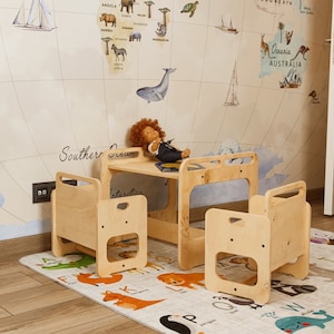 Puede incluir: Un conjunto de mesa y sillas de madera para ni&ntilde;os con un mapa del mundo en la pared detr&aacute;s. La mesa tiene un estante debajo y las sillas tienen respaldos abiertos. El conjunto est&aacute; sobre una alfombra con un patr&oacute;n de alfabeto.