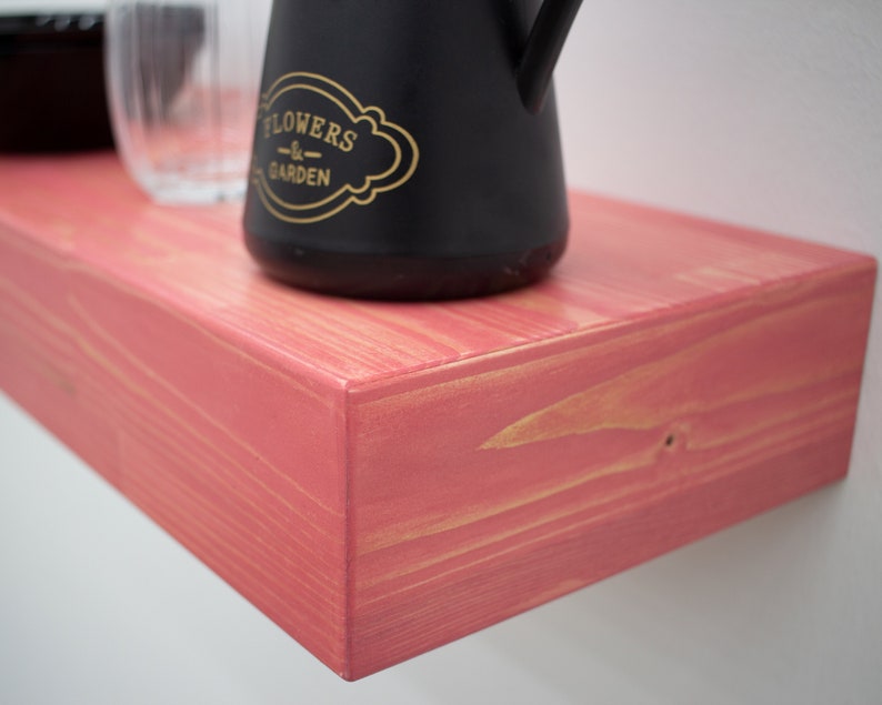 May include: A pink wooden shelf with a black watering can that says "Flowers & Garden" on it.